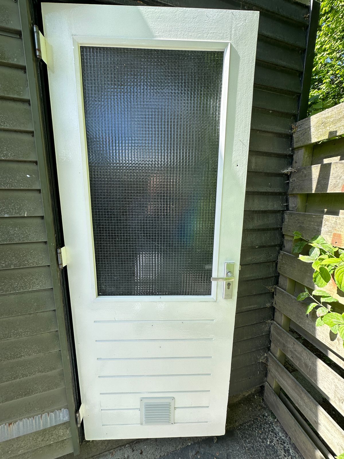Buitendeur na de restauratie: houtrot linksonder hersteld, nieuw ventilatierooster geplaatst en de hele deur strak wit geschilderd