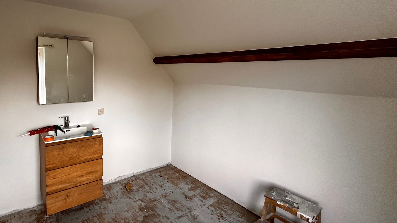 Zolderkamer na het stuc- en sauswerk: kopse wand, knieschot en dakschuinte egaal wit, met de bestaande houten gording in het zicht