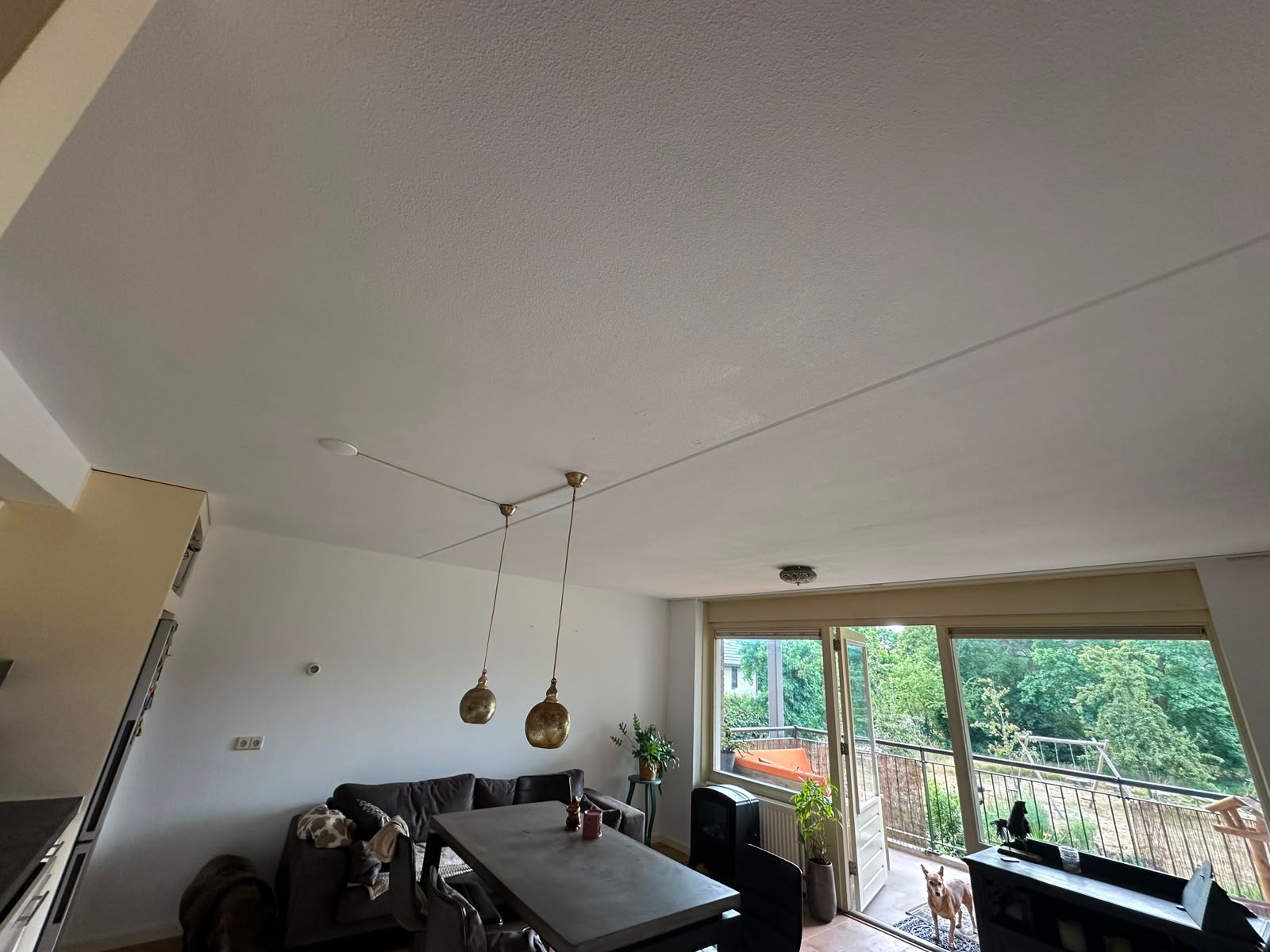 Woonkamer na het sausen: frisse witte muren en een egaal wit plafond; afdekraam, thermostaat en lampenkap weer gemonteerd